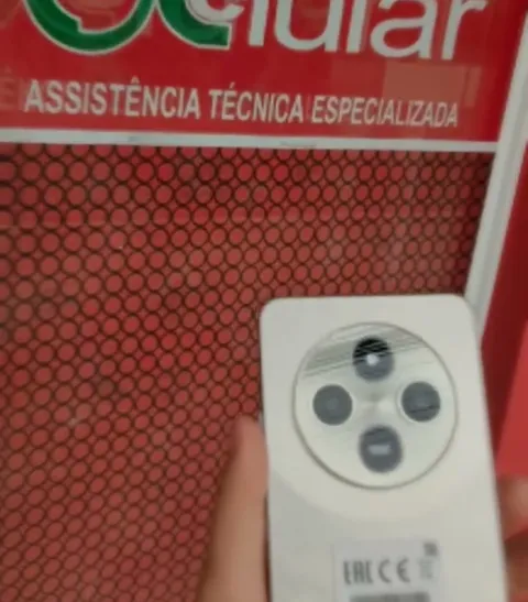 Celular na mão em frente ao letreiro vermelho da ÔCelular